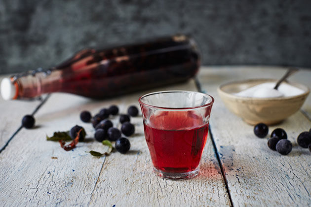 How to make sloe gin - a glass of sloe gin with sloes scattered on the table behind it