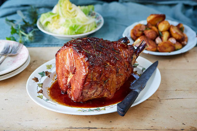 roast glazed pork with roast potatoes in the background and salad