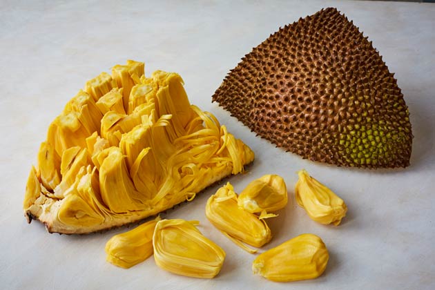 A jackfruit cut in half, the inside showing the 'meat of the fruit' and half showing the outside