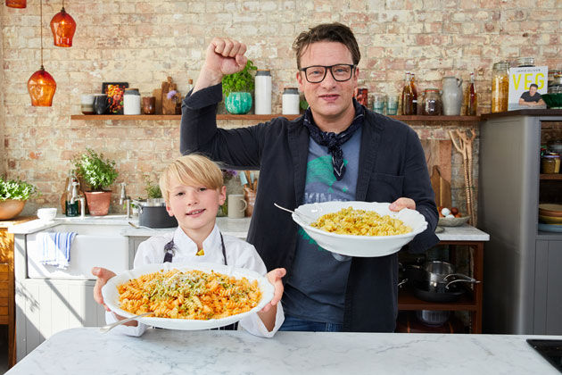 Buddy holding a large plate full of pasta next to Jamie holding another bowl punching the air with his fist