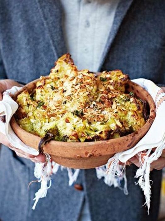 person holding a terracotta pot full over baked broccoli and cauliflower cheese