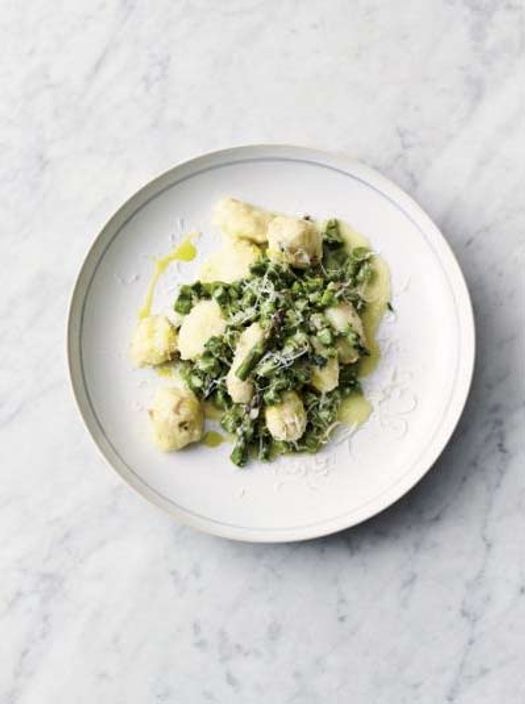 A white plate with a pile of gnocchi and asparagus on a marble table