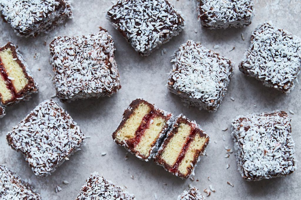 Lots of coconut-coated Lamingtons from Australia. Some cut in half revealing a layer of red jam sandwiched between the sponge.
