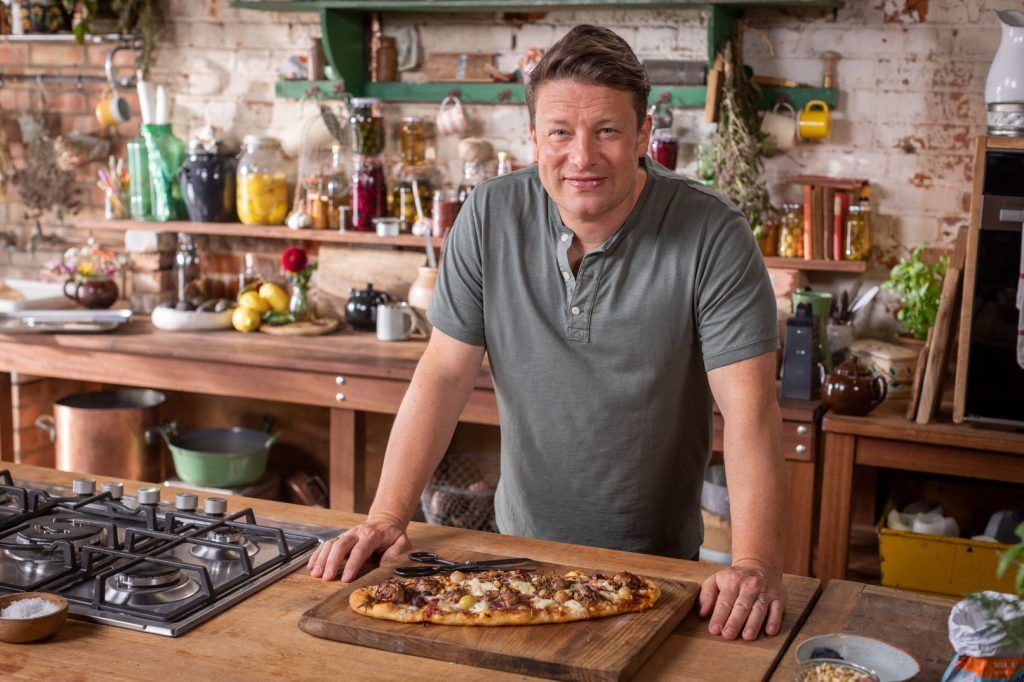 Jamie standing in the kitchen in front of a sausage pizza, a perfect freezer-friendly meal