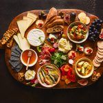 Grazing board ideas – an array of savoury food on a wooden board including cheeses, meats, olives and crackers