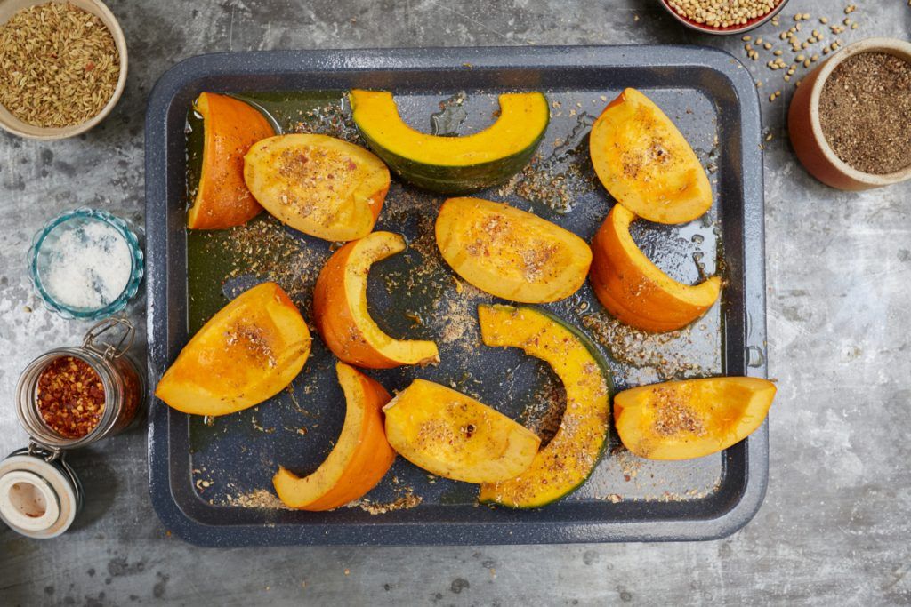 Pumpkin chopped into wedges on a baking tray, ready to go into the oven with spices to create a gorgeous roasted pumpkin recipe