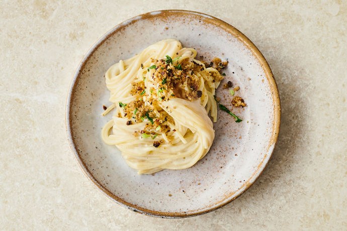 Plate of spaghetti in a white cauliflower cheese sauce topped with crispy cauli leaf bread crumbs