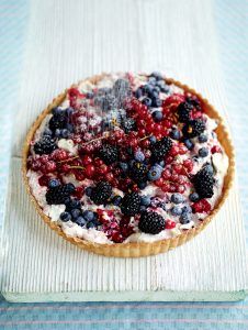 Colourful berry tart filled with creamy and topped with blueberries, cranberries, loganberries and more