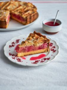 A wedge of pie layered with golden custard and pink stewed rhubarb, served with a pot of berry compote