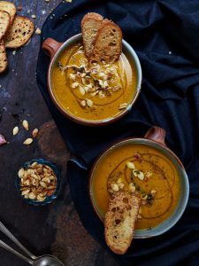 Two bowls of pumpkin soup with seeds and crusty bread