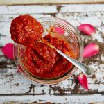 Best harissa recipes – a jar of red harissa paste being spooned out, with rose petals on the table around it