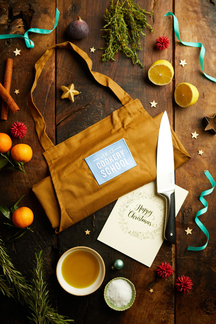 A Jamie Oliver Cookery School apron, gift voucher and knife with lemons, clementines and Christmas decorations around it