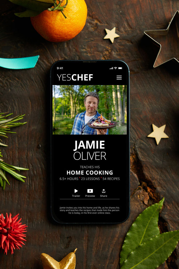 A mobile phone displaying Jamie's YesChef page on the screen. The phone is surrounded by pine leaves, stars and ribbons