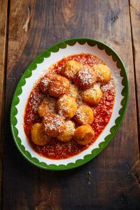 A plate of potato bombs on a bed of tomato sauce, with Parmesan shavings on top