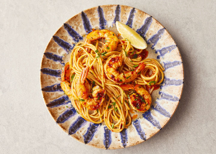 A plate of spaghetti with king prawns, a lemon wedge and parsley on top