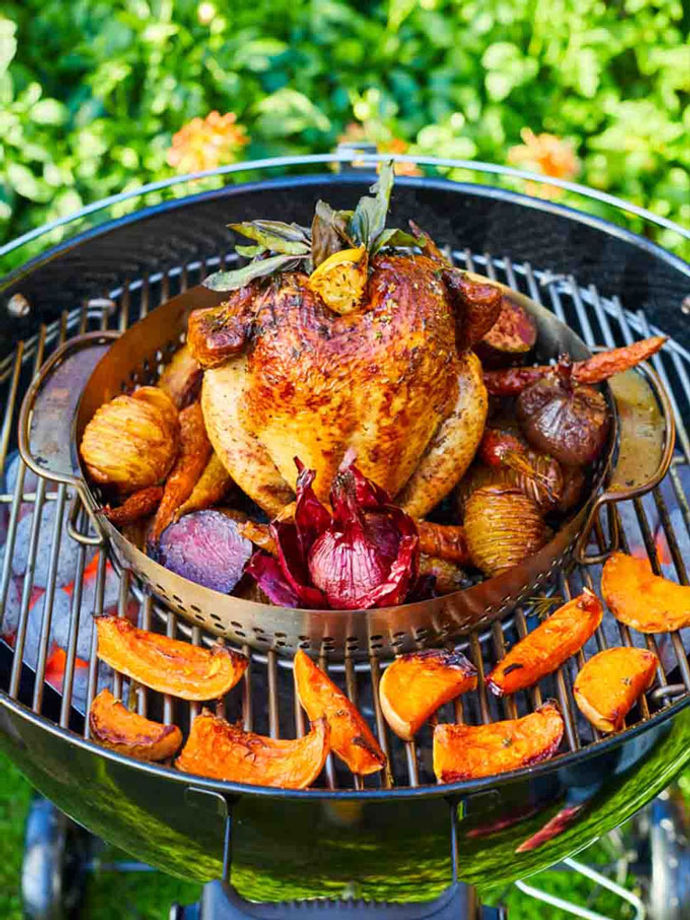 Whole chicken on a Weber barbecue with veggies and herbs on top