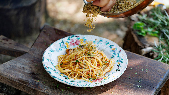 A bowl of spaghetti arrabbiata with Jamie sprinkling herby, crispy breadcrumbs on top