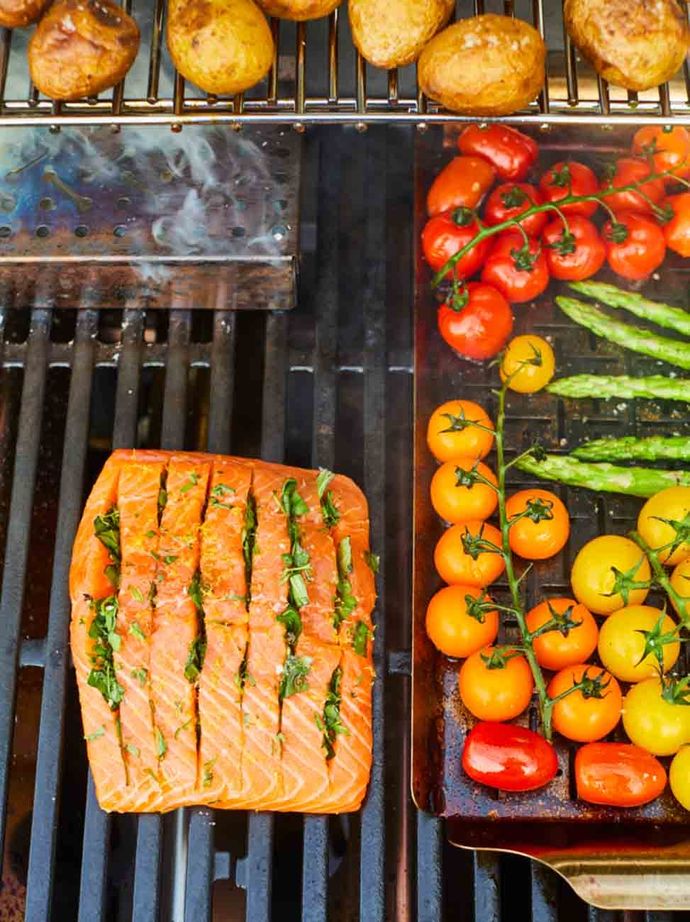 Crispy salmon with tomatoes, asparagus and potatoes, being grilled on a Weber barbecue