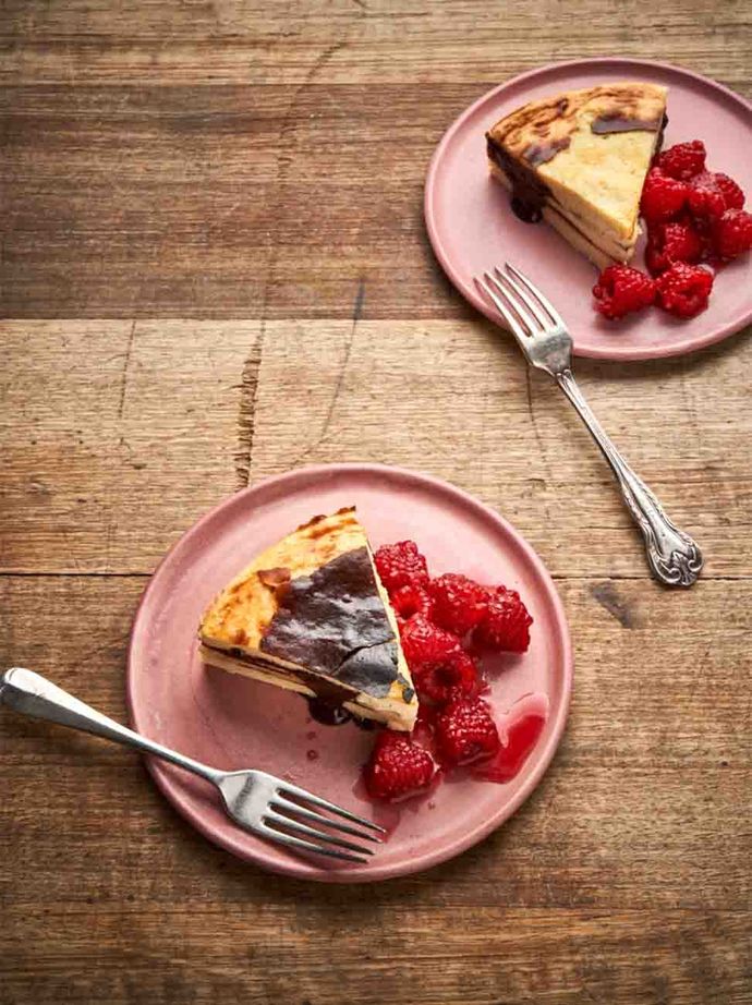 A wedge of Basque-style cheesecake with a nearly-burnt top, served on a plate with raspberries