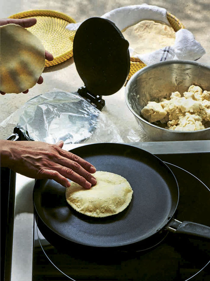 A pair of hands in frame, making corn tortillas