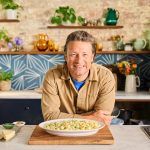 Jamie Oliver smiling at the camera with a large plate of % ingredient sweet pea orecchiette in front of him. A great midweek meal