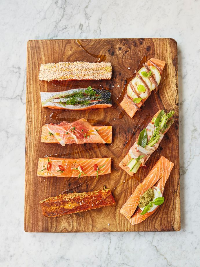 8 filets of salmon on a wooden block. Each fillet has a different topping. From Simply Jamie cookbook