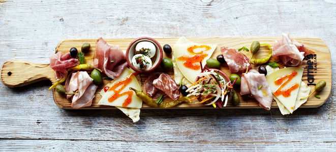 wooden board with a selection of cheeses, olives, hams and eggs on it