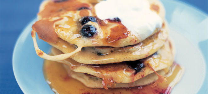 a stack of blueberry pancakes with cream and butter on top