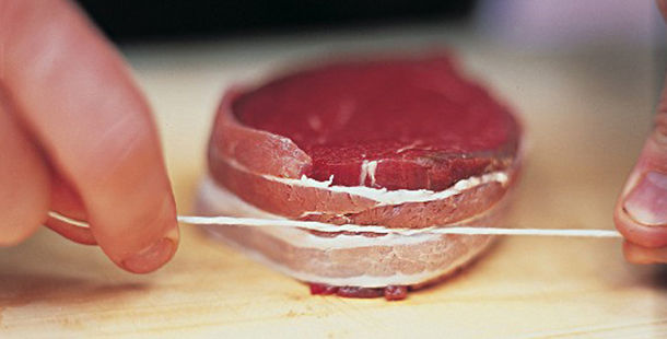 raw meat being tied up with string by butcher