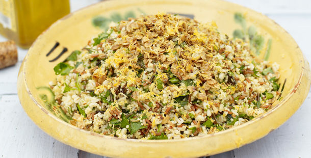 a bowl full of grains with chopped herbs and salad leaves