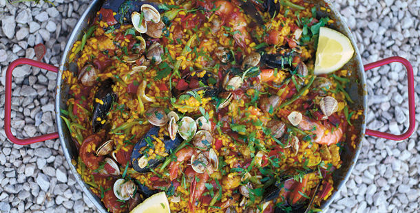 paella in a metal dish with lemon slices and mixed seafood