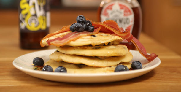 stack of blueberry pancakes with syrup and bacon on top