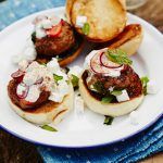 lamb sliders on top of a bread bun with sour cream and feta