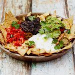 perfect nachos with herbs, guacamole, chilli, sour cream and refried beans