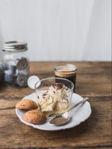 A clear coffee cup filled with ice cream, coffee and chocolate sprinkles for the perfect affogato recipe. There's biscotti and a spoon on the side.