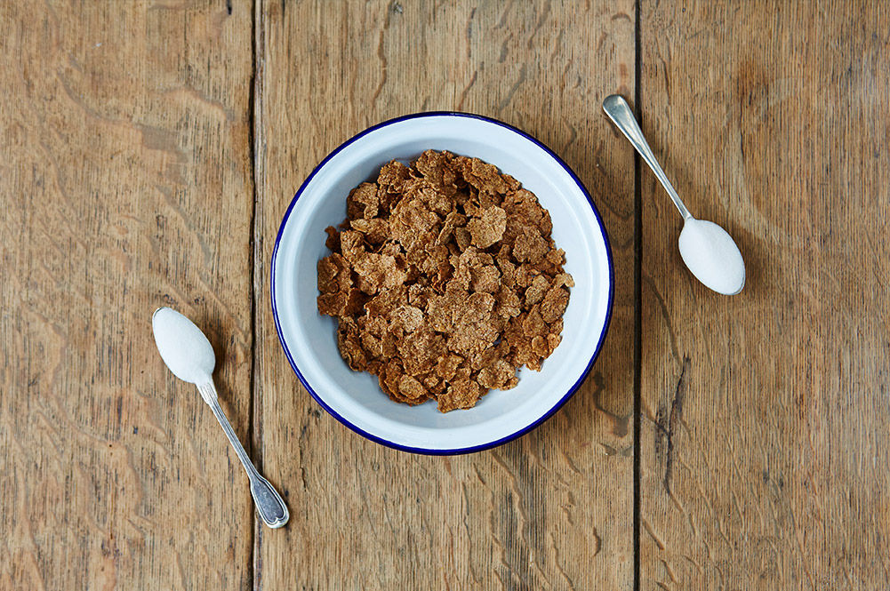 bran flakes cereal with 2 spoons of sugar next to it
