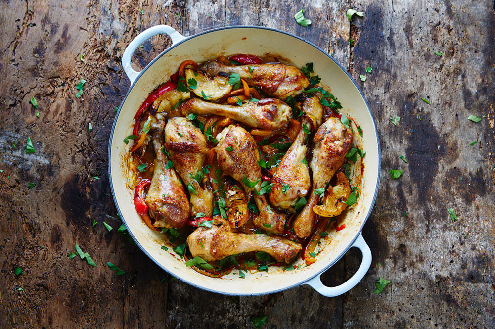 chicken legs roasted in a pan with lemon wedges and herbs