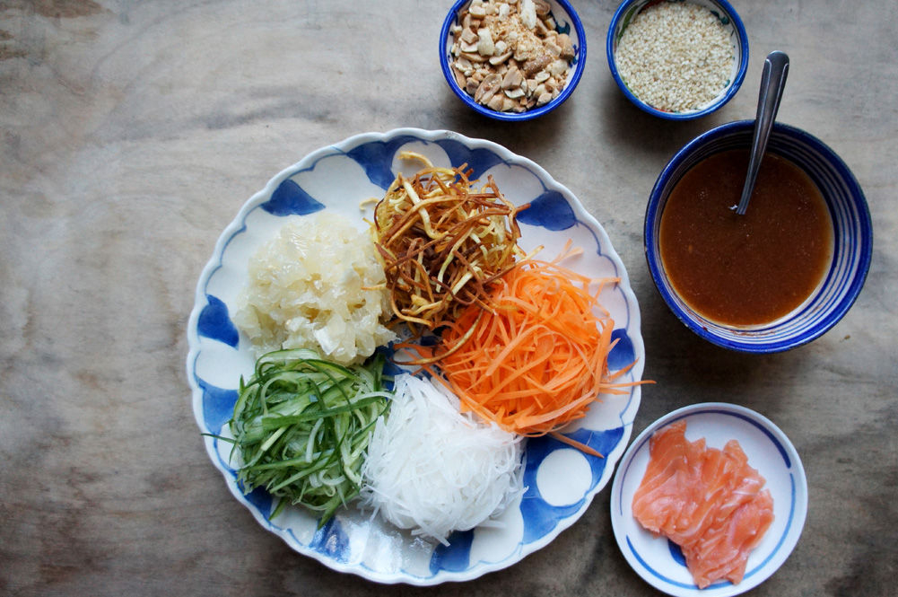 bowl of yu sheng, shredded vegetables with salmon and sauces next to it