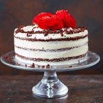 red velvet cake on a stand with roses on top