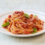 tomato spaghetti on a plate with basil on top