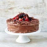 chocolate cake with berries on top and on a cake stand with chocolate shavings