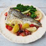 fish on a plate with greens and lemon slices