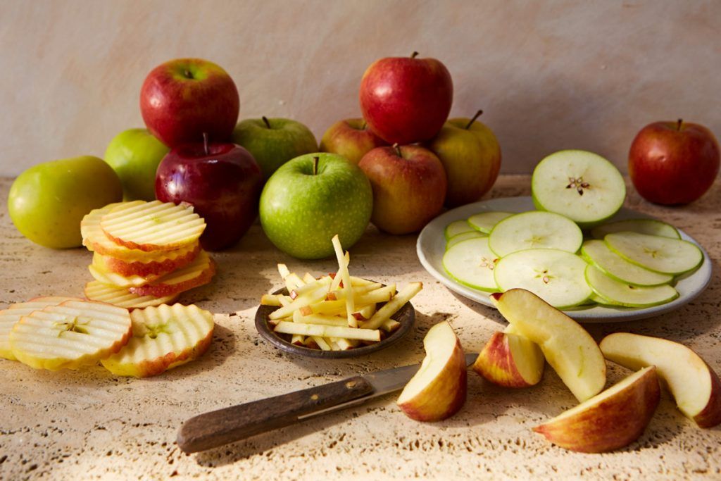 a variety of apples sliced in different ways with different knives