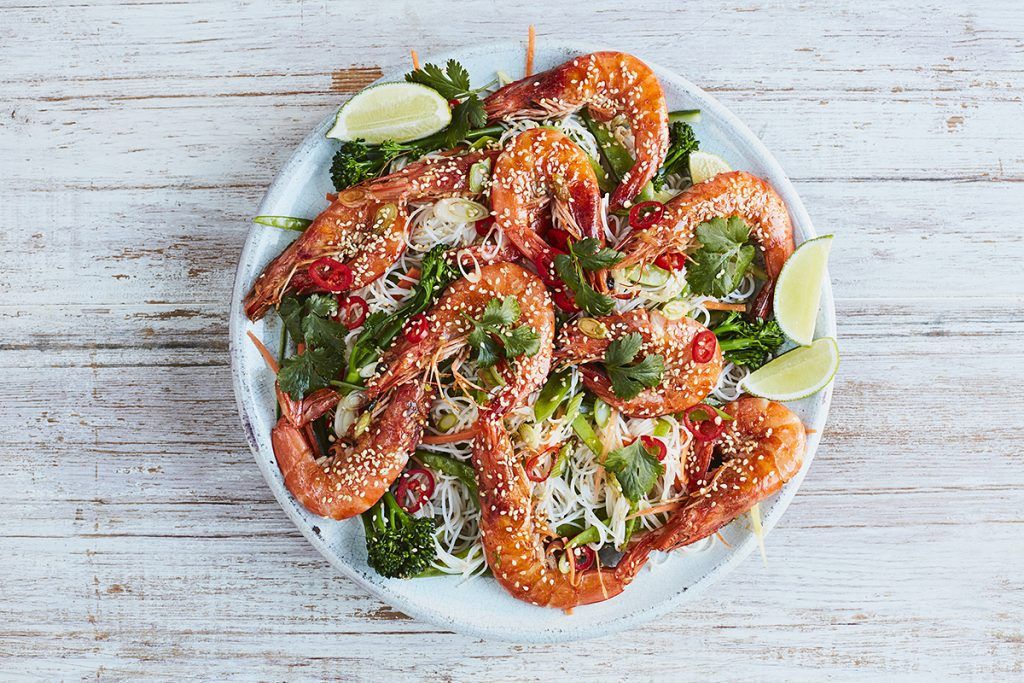 prawns covered in sesame seeds in a noodle spring onion salad and slices of lime