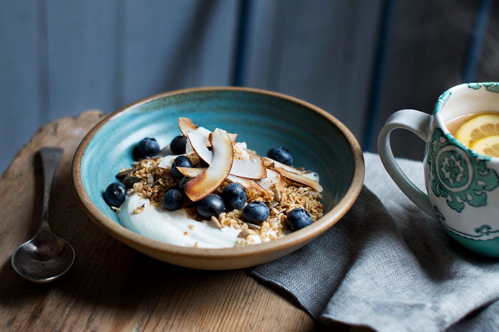 granola, oats, coconut shavings, blueberries and yoghurt in a bowl with lemon tea on the side