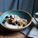 granola, oats, coconut shavings, blueberries and yoghurt in a bowl with lemon tea on the side