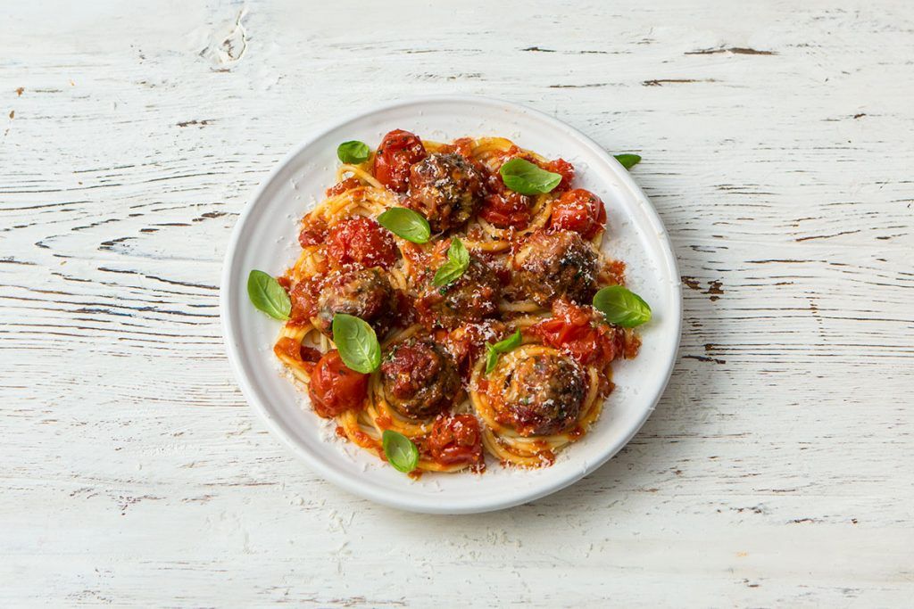 Spaghetti and meatballs in tomato sauce with basil on top