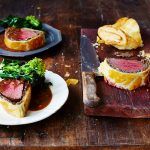 beef wellington recipe on board sliced in sections with gravy and broccoli