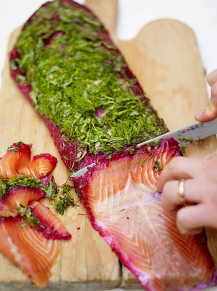 salmon being sliced with herbs on top