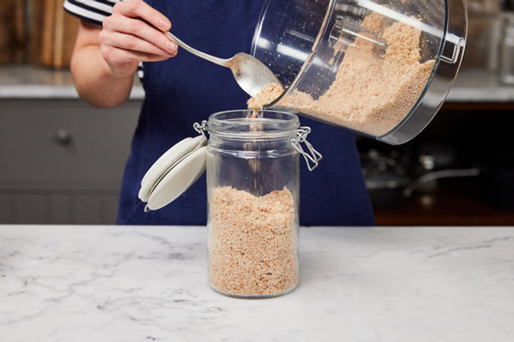 Hands transferring breadcrumbs from food processor into a jar